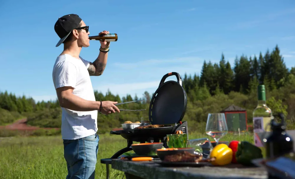 man outside barbecueing and drinkin beer