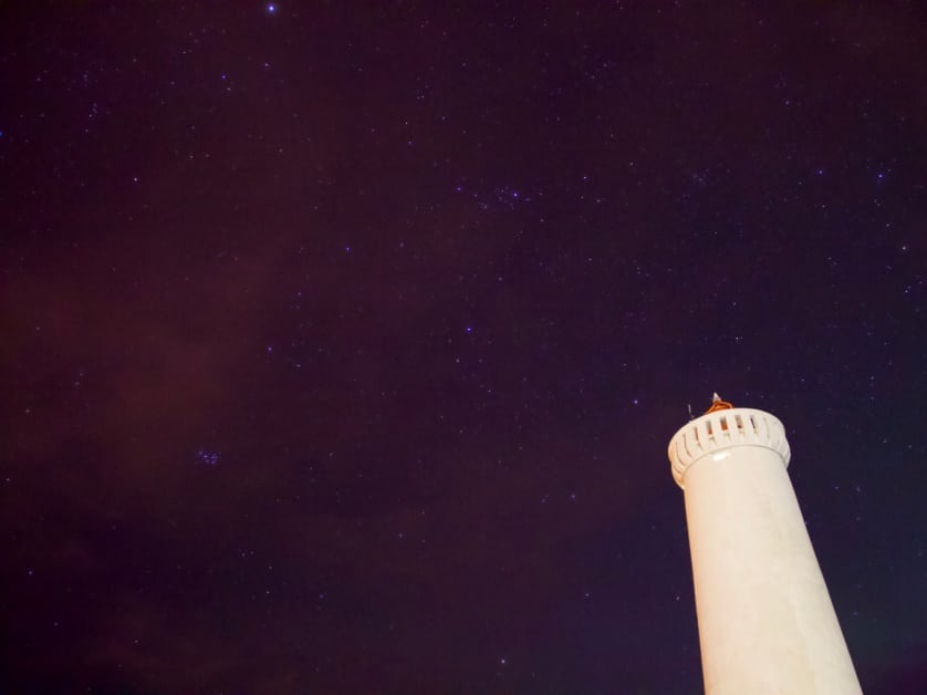 A lighthouse juts against a deep purple night sky with pink and purple stars.