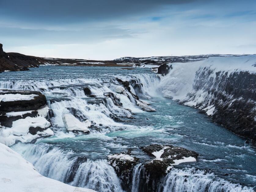 Gorgeous white water of the Gulfoss waterfall flows over black stone during winter.