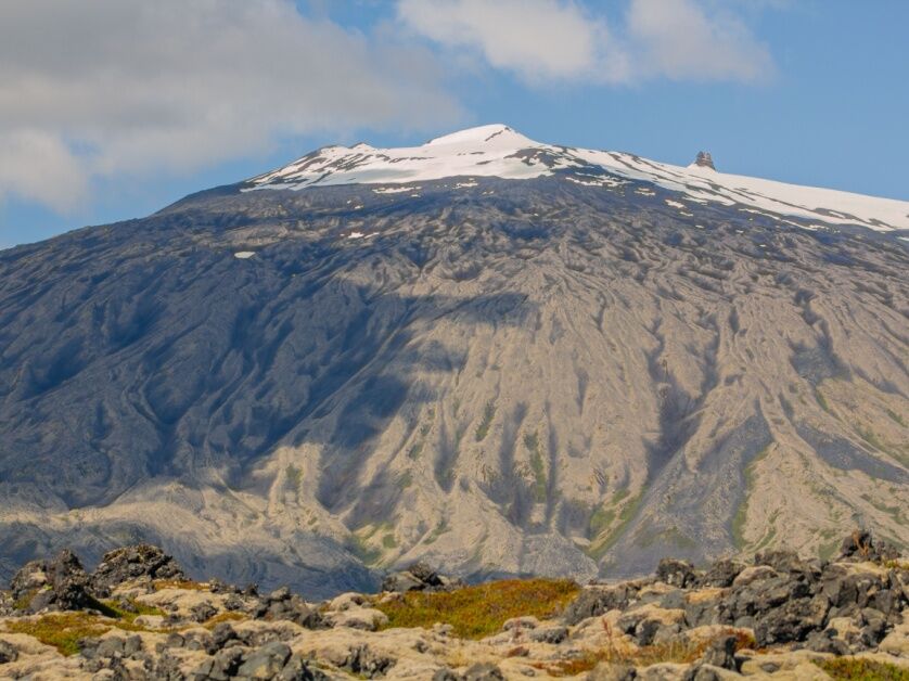 Snæfellsjökull’s glacier towers like a mountain, its peak snowcapped and surrounded by rocks and grass.