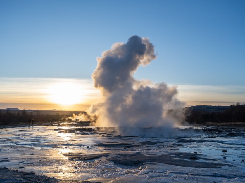 The Strokkur Geysir, frozen in time during an eruption with the golden Icelandic sun lighting its mists and the ground around it.